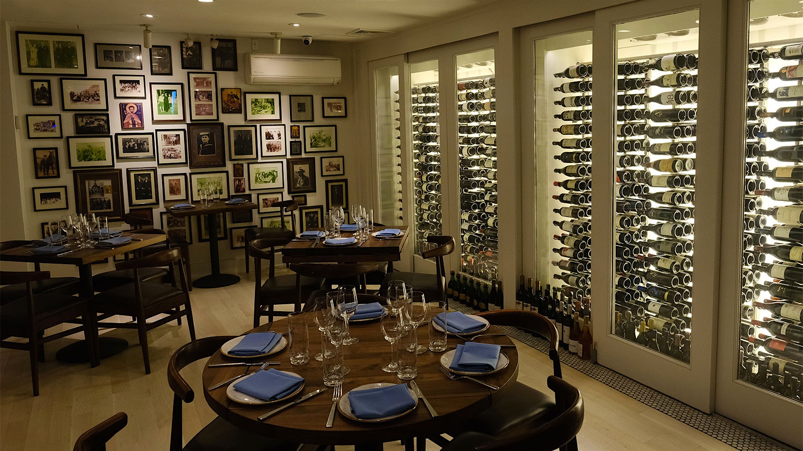  A view of the dining room at Molyvos' new location in Hell's Kitchen, with wine prominently displayed and artwork and ceramic plates on the walls